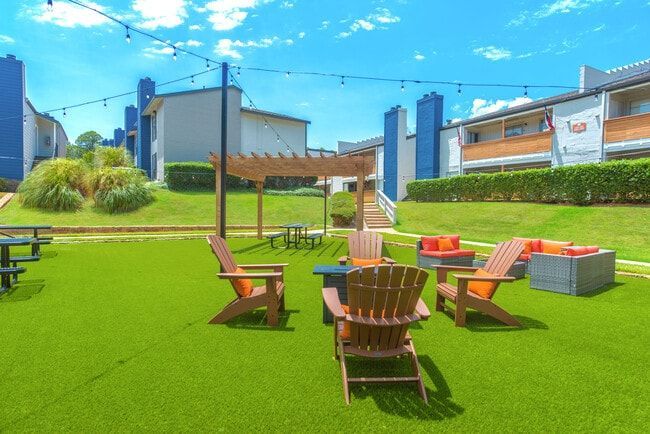 Outdoor seating area with Adirondack chairs, a pergola, and string lights on a grassy lawn.