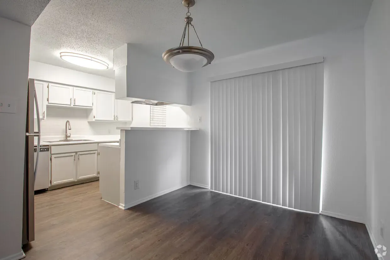 White kitchen and dining area with wood-look floor. Appliances, cabinets, and bar separate from dining area with sliding door.
