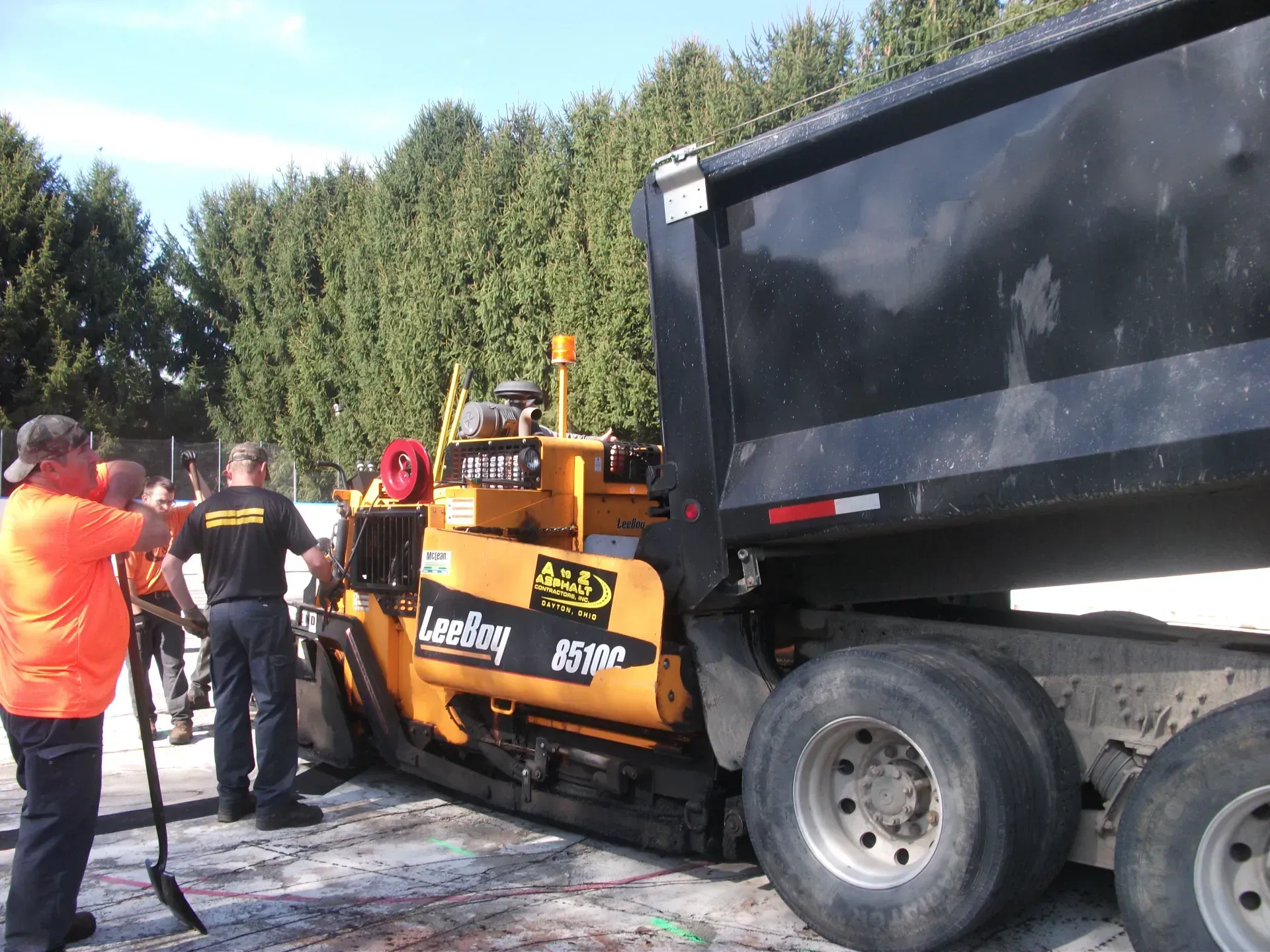 A man in an orange shirt is standing next to a large dump truck