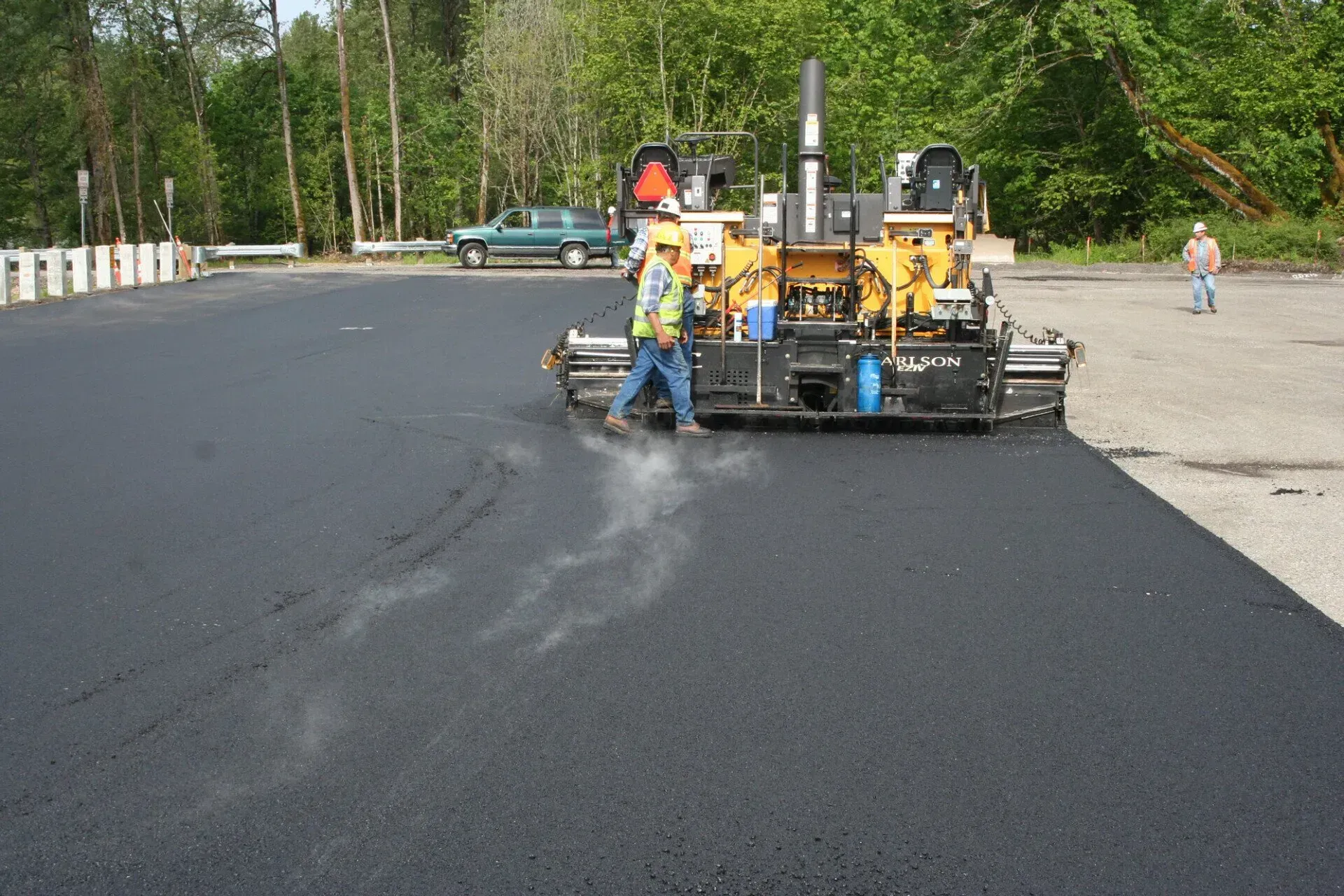 A man walking next to a machine that is laying asphalt