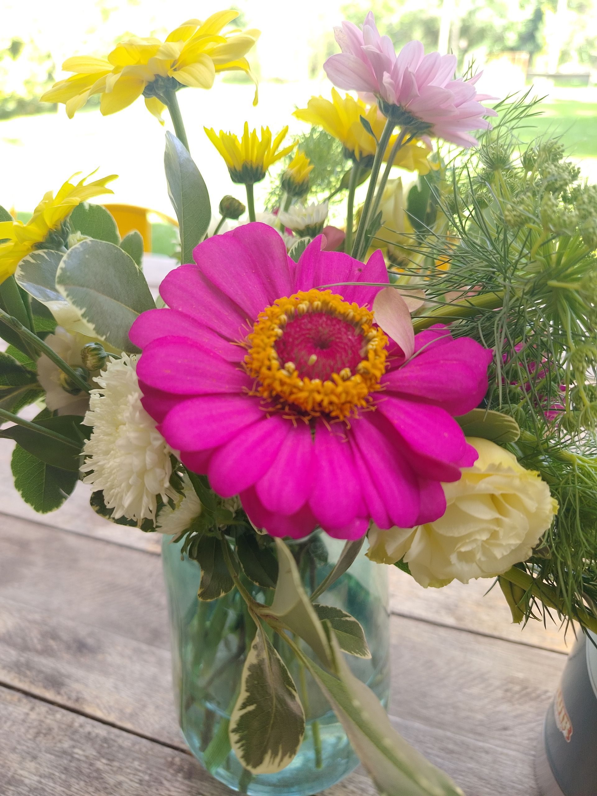 Zinnia rosa y margaritas amarillas en un jarrón de vidrio sobre una mesa de madera.