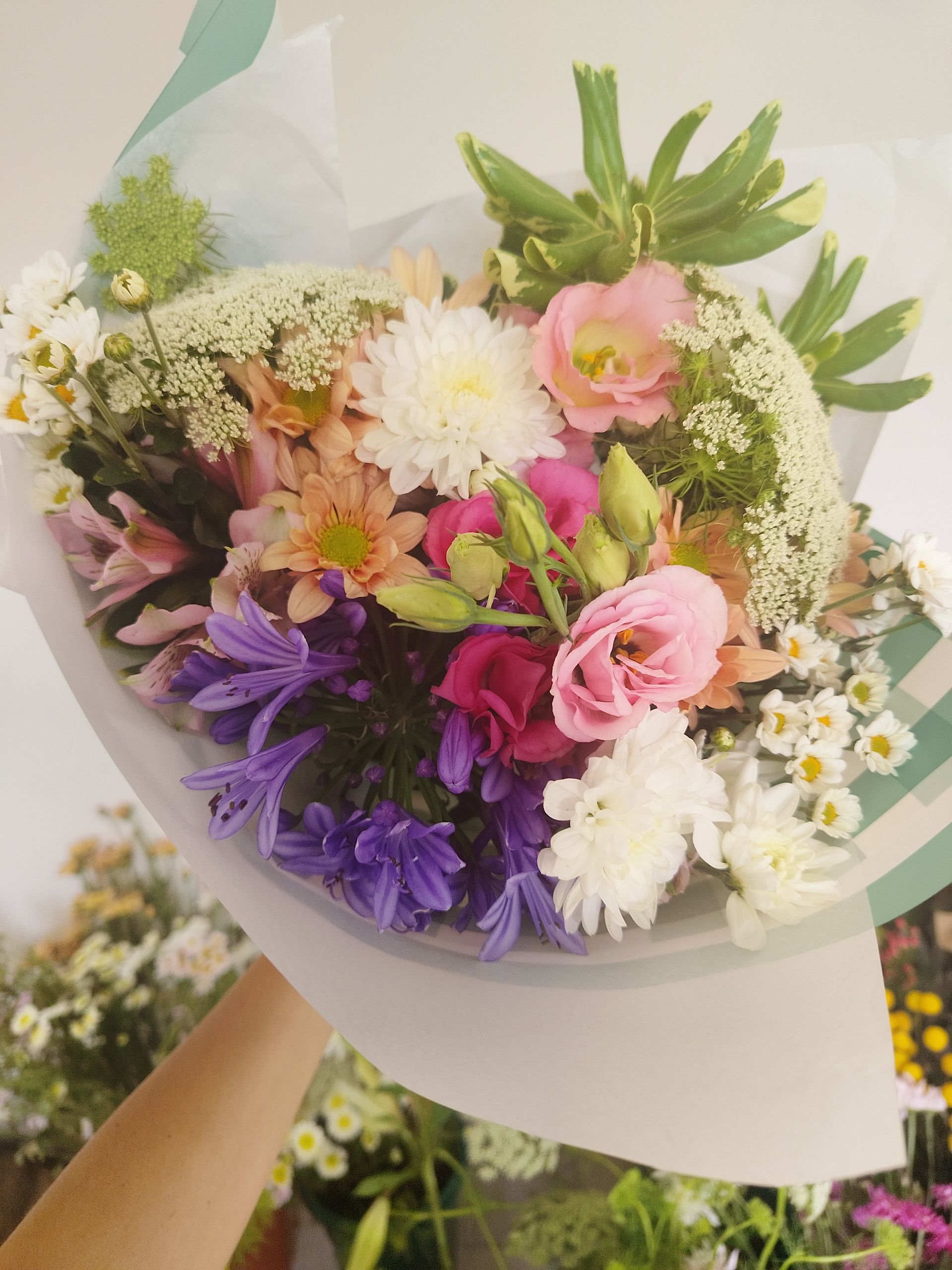 Ramo de flores de colores envuelto en papel de rayas blancas y verdes, sostenido por una persona.