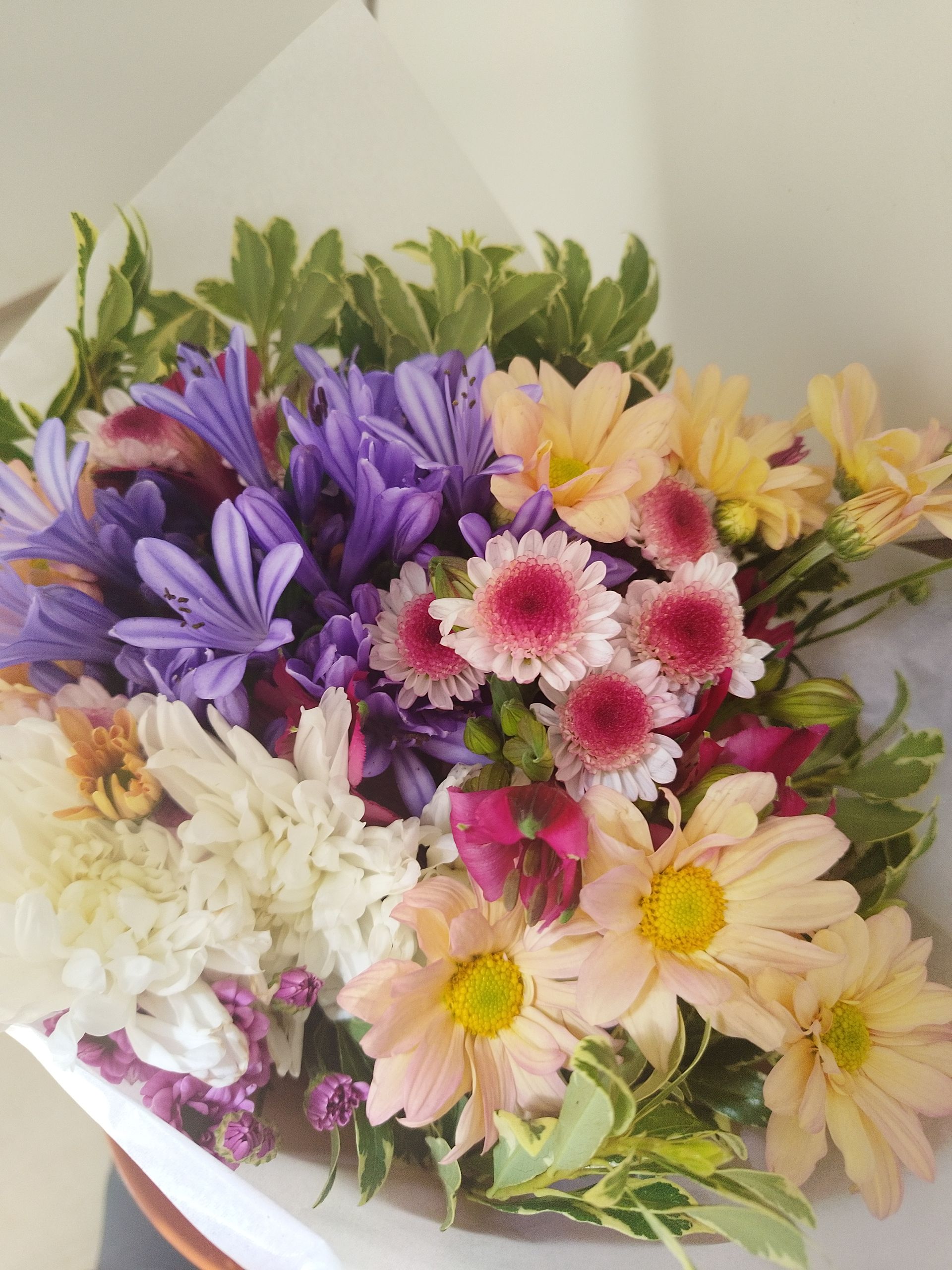 Ramo colorido de flores, que incluye flores de color púrpura, rosa y amarillo, envuelto en papel.