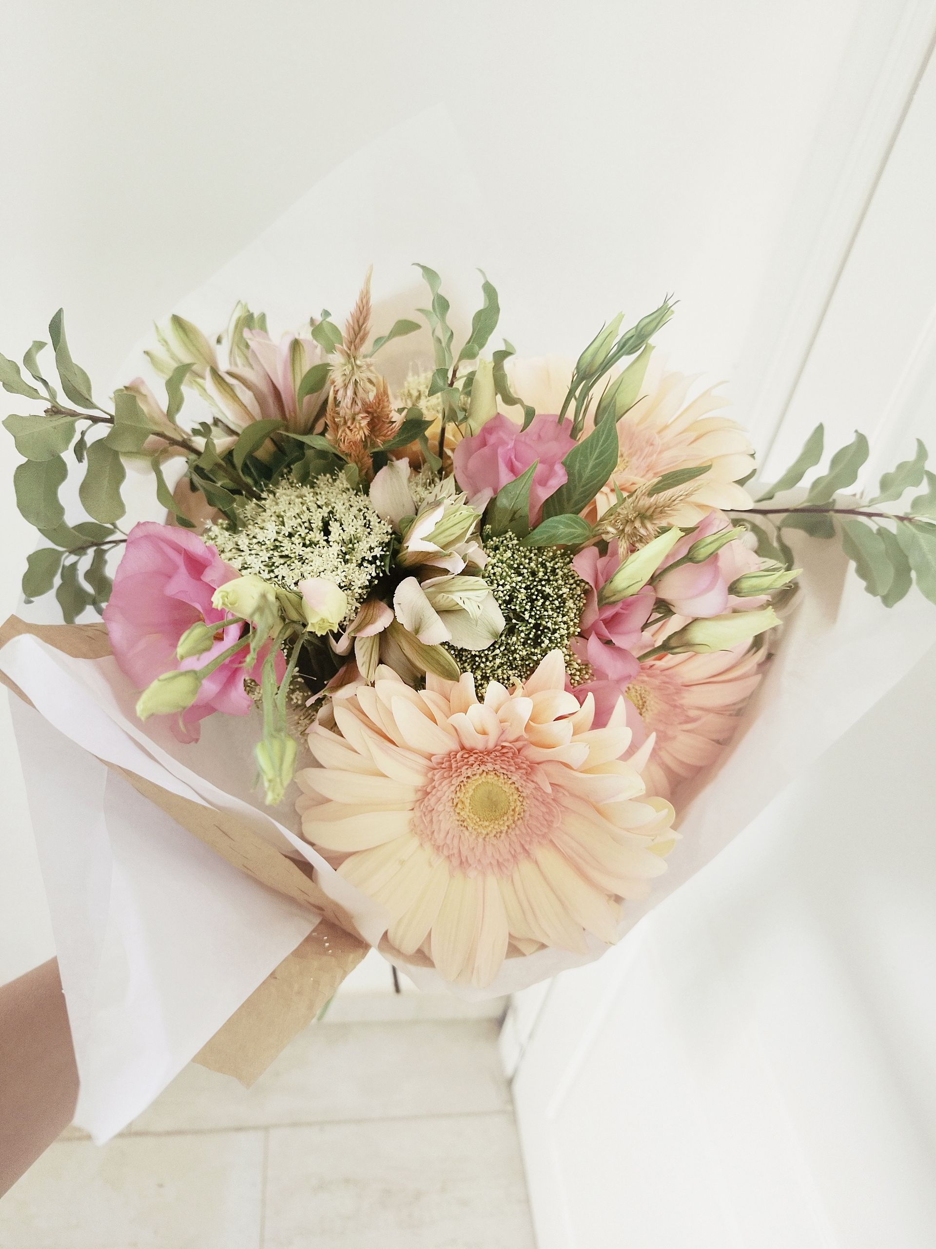 Ramo de flores de color melocotón y rosa envuelto en papel blanco y tostado.