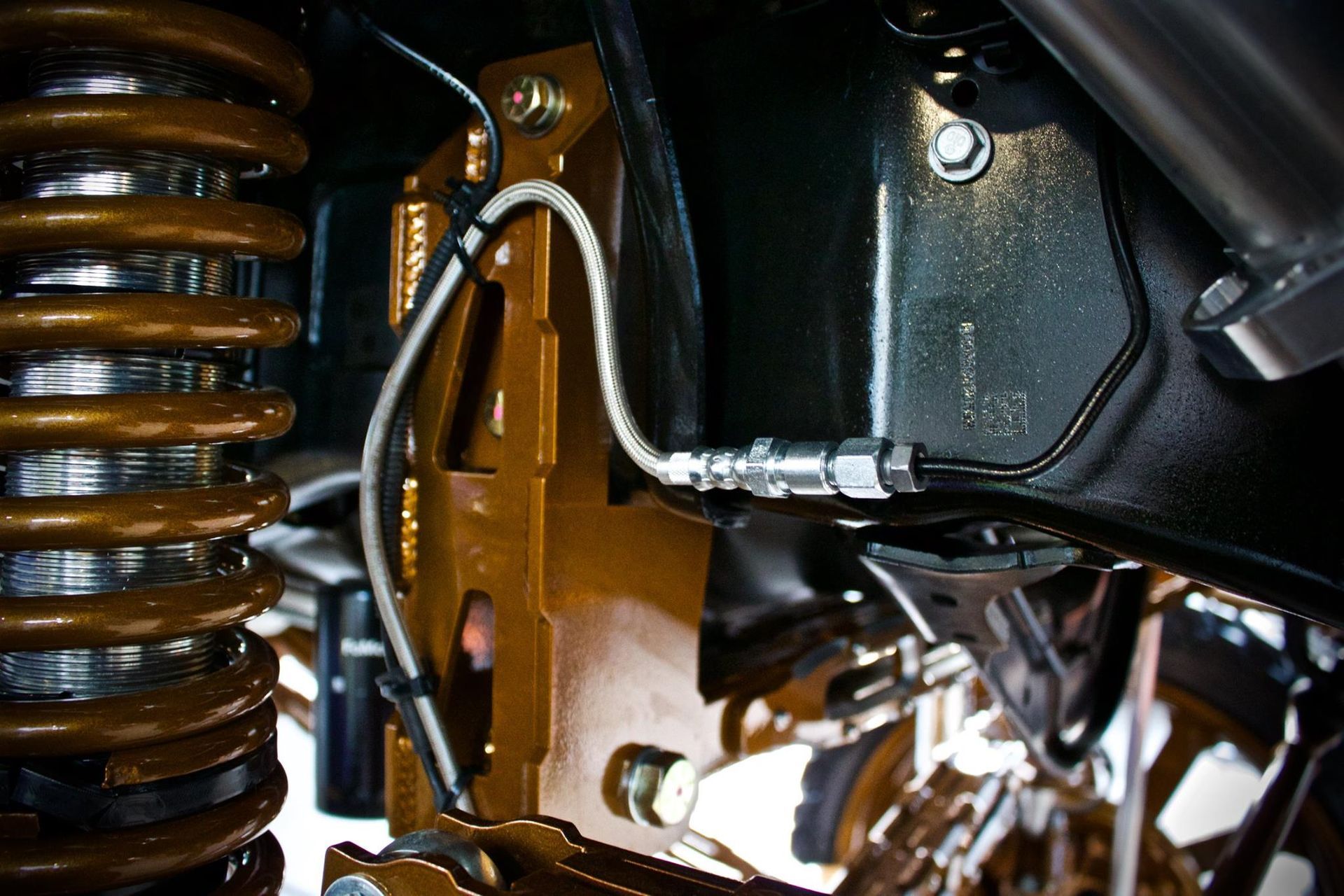 Close-up of a car's brake disc with drilled holes, caliper, and mounting hardware, likely during vehicle assembly.