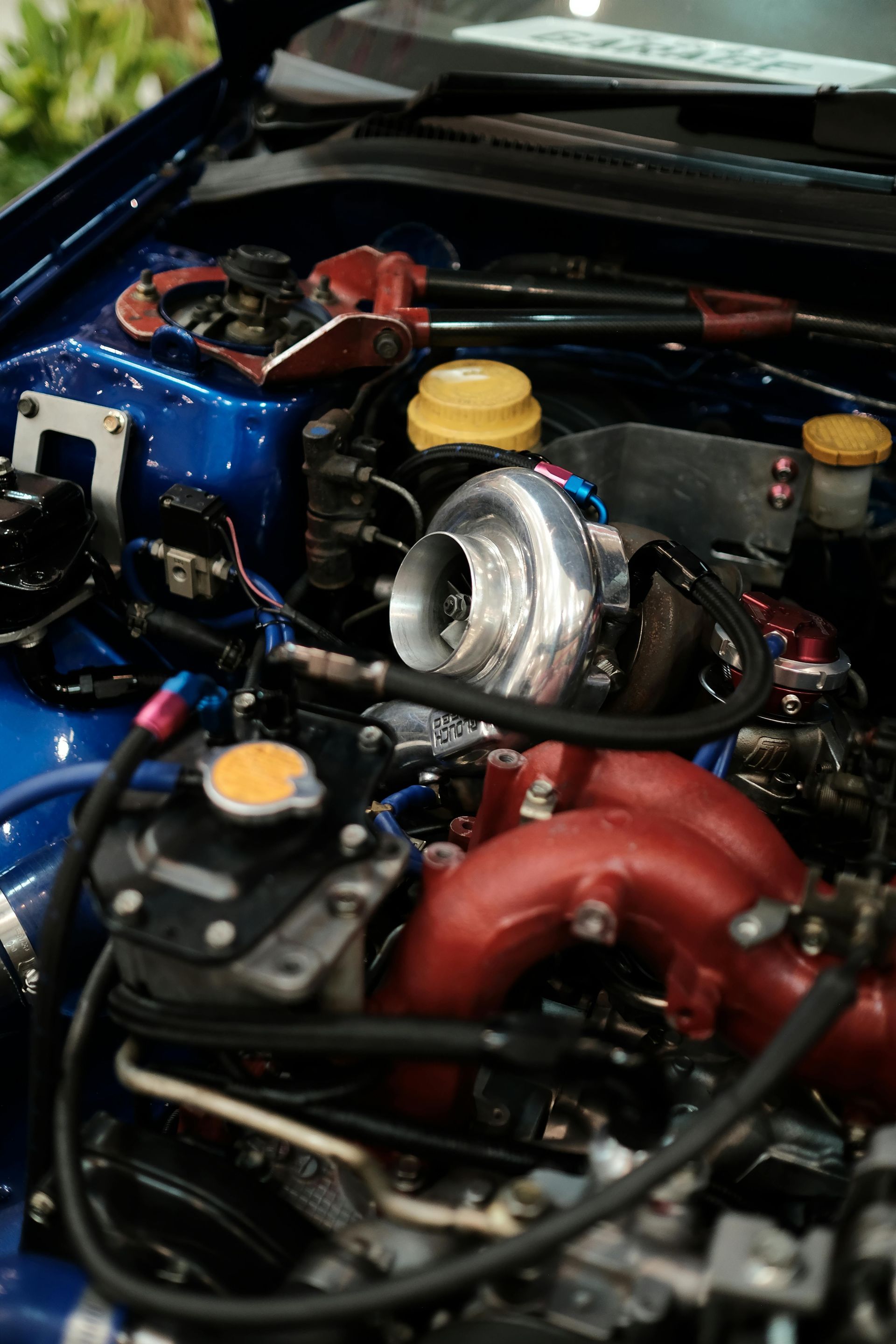 Blue car engine bay with red intake manifold and silver turbocharger.
