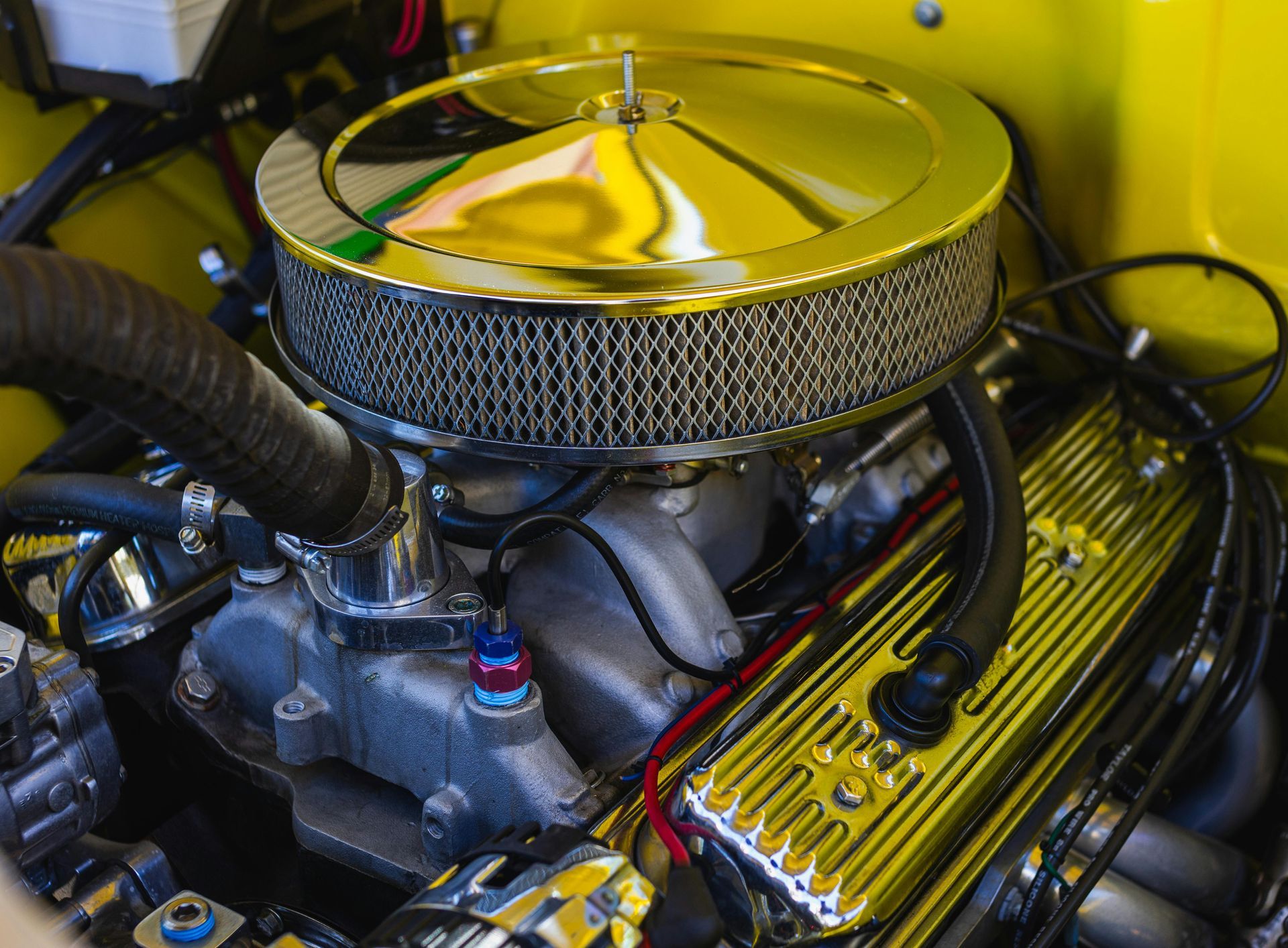 Yellow classic car engine hoses with chrome air filter and valve covers.