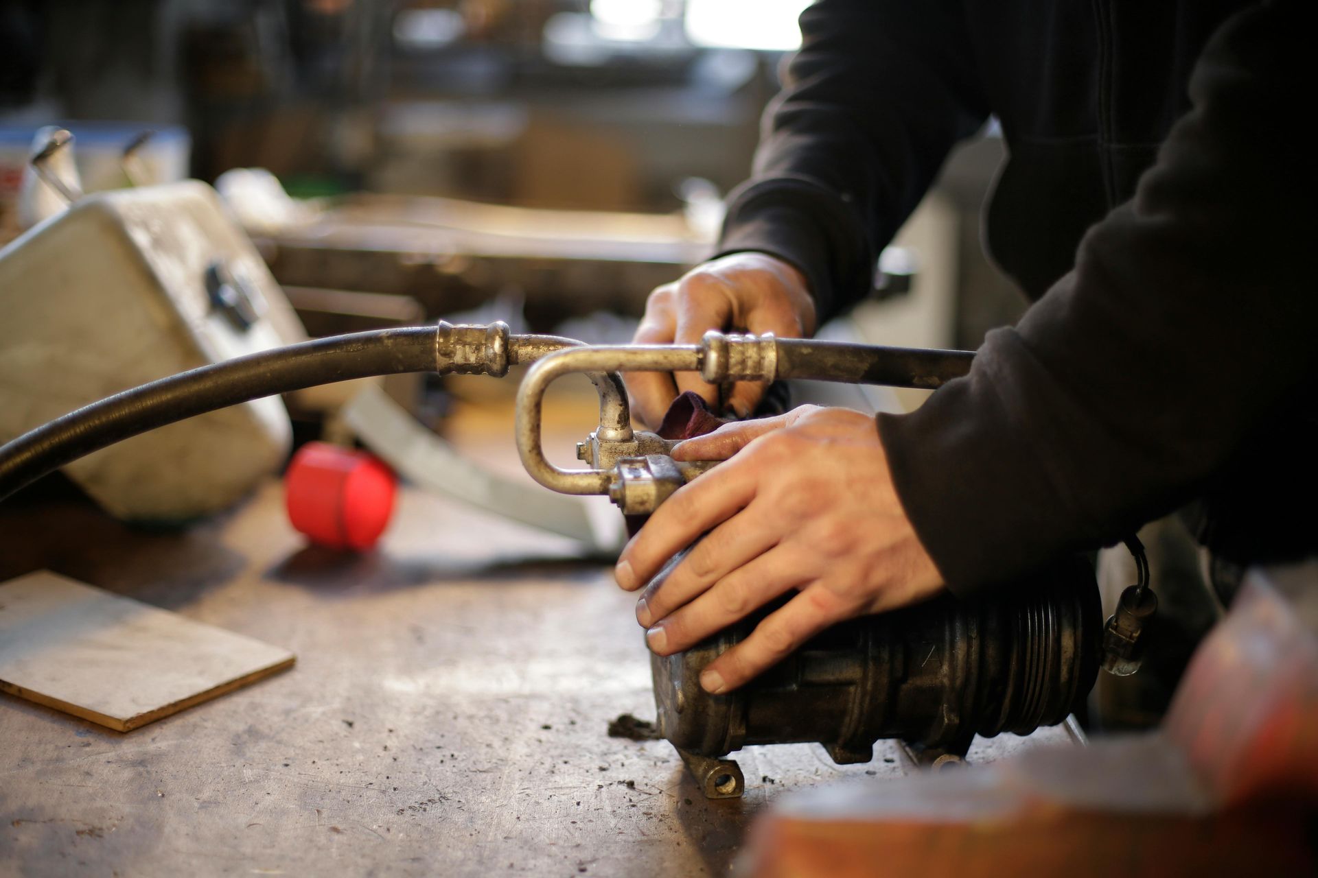 Man in blue jumpsuit connects a metal fitting to black hoses in a workshop.