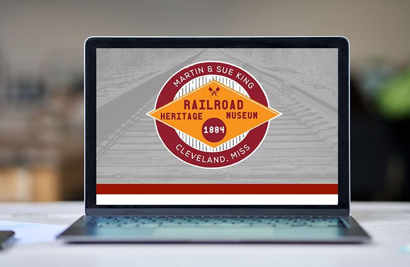 A laptop computer is sitting on a table with a railroad heritage museum logo on the screen.
