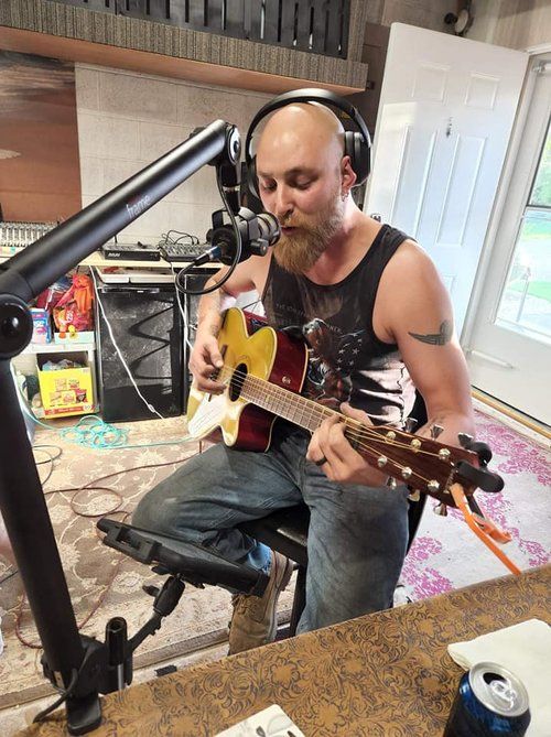 A man wearing headphones is playing a guitar in front of a microphone.