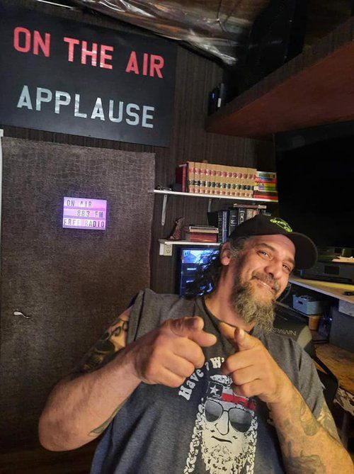 A man giving a thumbs up in front of a sign that says on the air applause