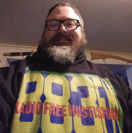 A man with a beard is wearing a shirt that says radio free hustford