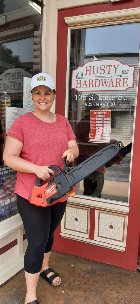 A woman is holding a chainsaw in front of a hardware store.