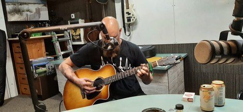 A man with a beard is sitting at a table playing an acoustic guitar.