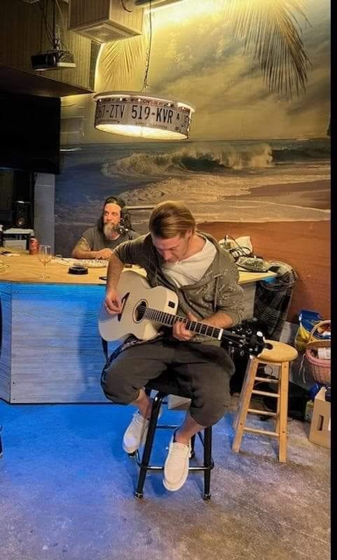 A man is sitting on a stool playing a guitar in a room.
