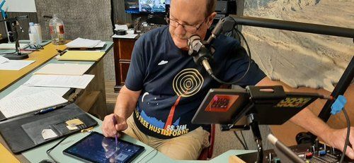 A man is sitting at a desk with a microphone and a tablet.