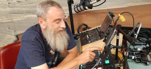 A man with a beard is sitting in front of a microphone in a studio.