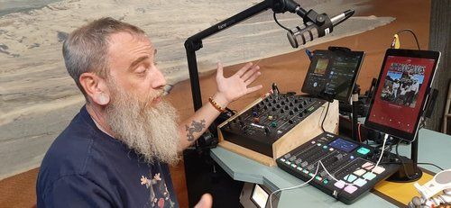 A man with a beard is sitting at a table in front of a microphone.