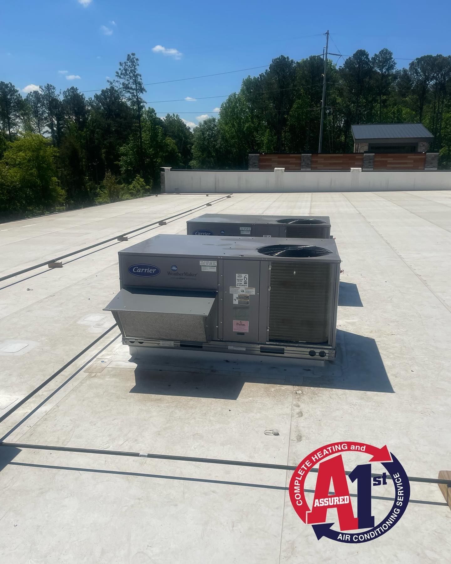 Two rooftop Carrier HVAC units on a concrete roof with trees in the background.