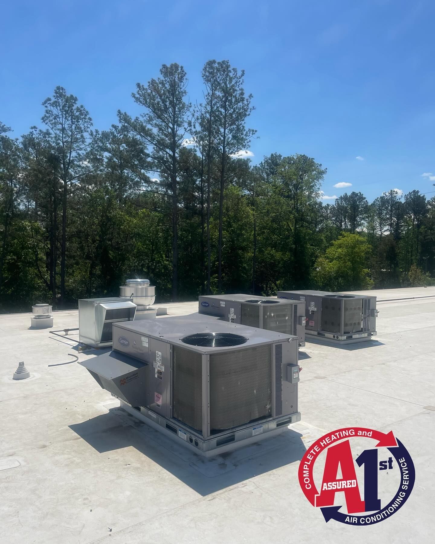 HVAC units on a rooftop against a backdrop of trees and a blue sky.