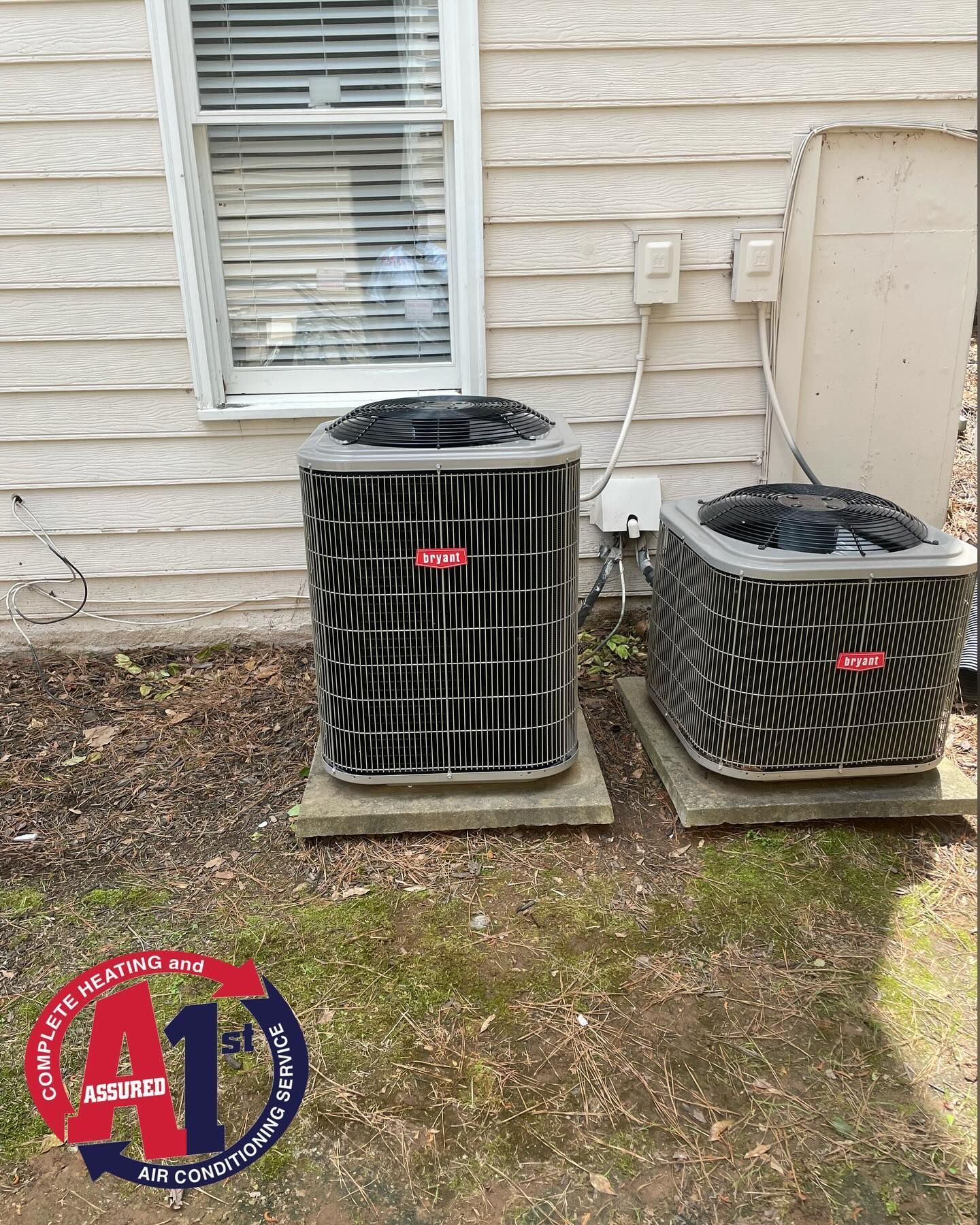 Two Bryant air conditioning units sit outside a building next to a small window.