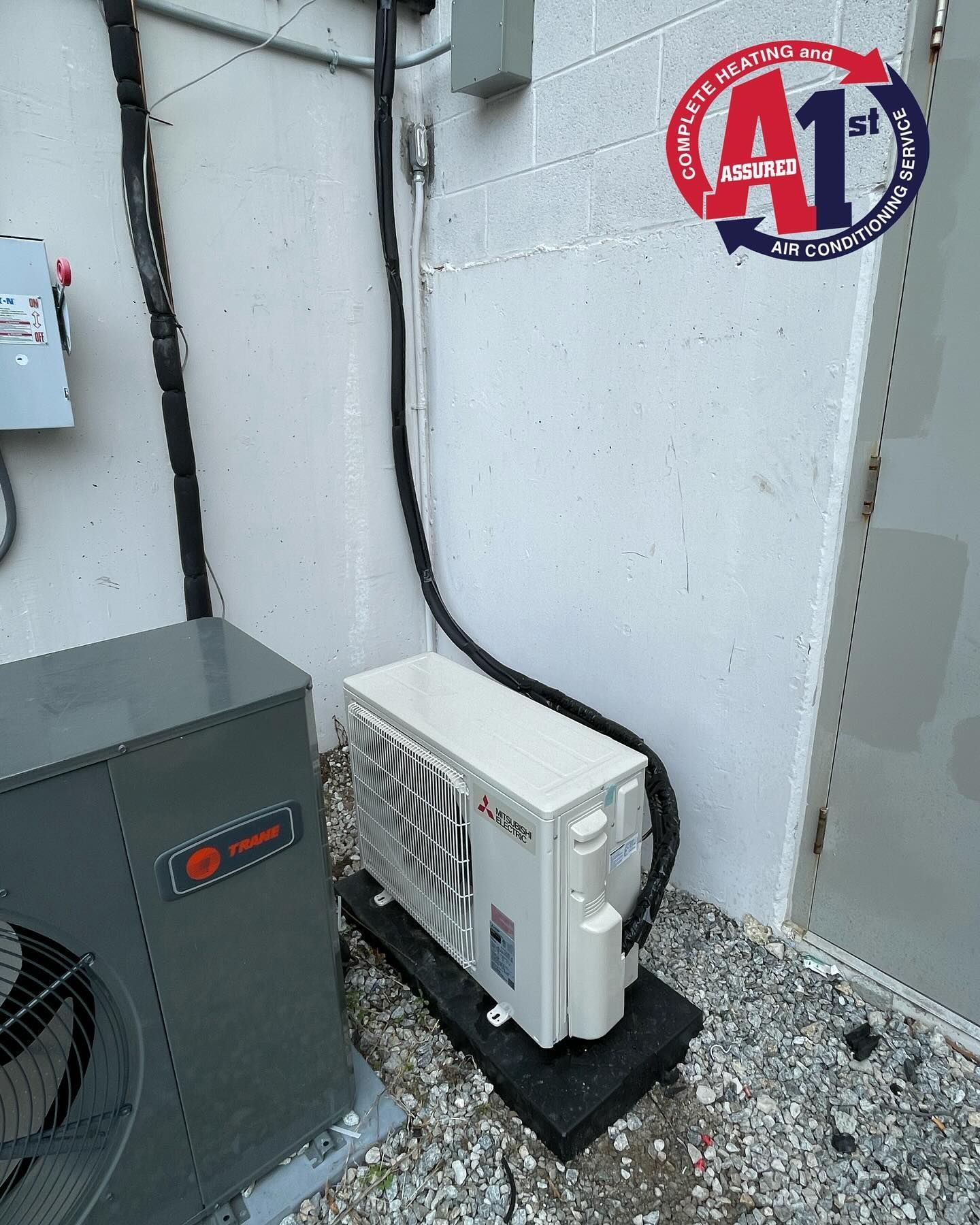 Outdoor HVAC units against a white wall; an air handler sits on a black platform.