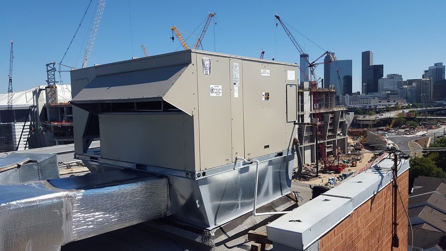 Rooftop HVAC unit on a building with city skyline and construction cranes in the background.