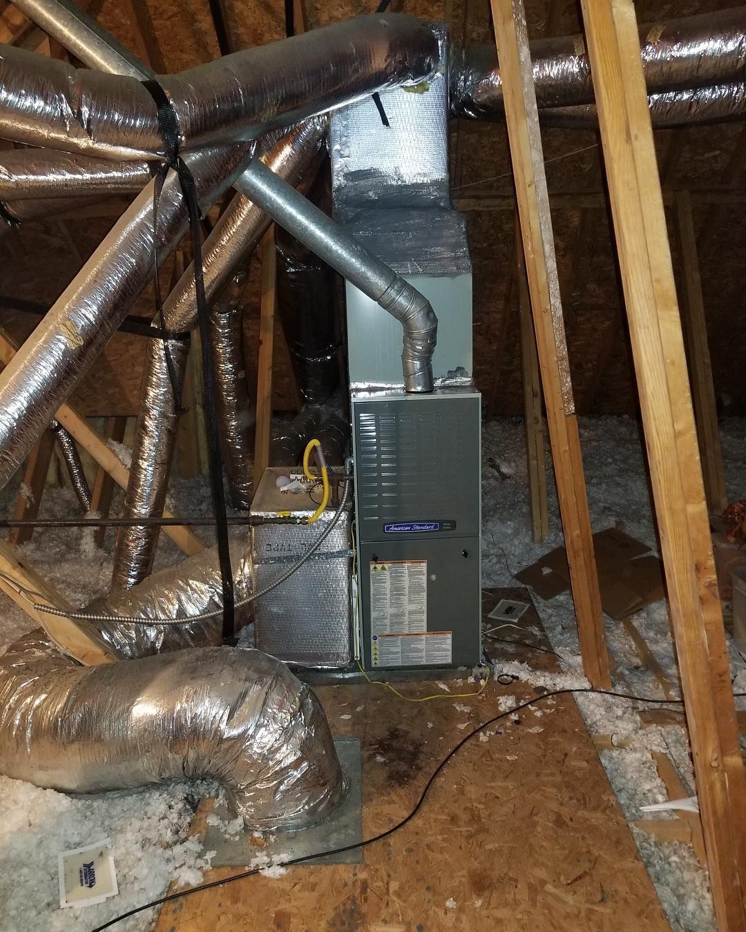 Furnace and ductwork in an attic, with metallic, insulated tubes and wooden supports.