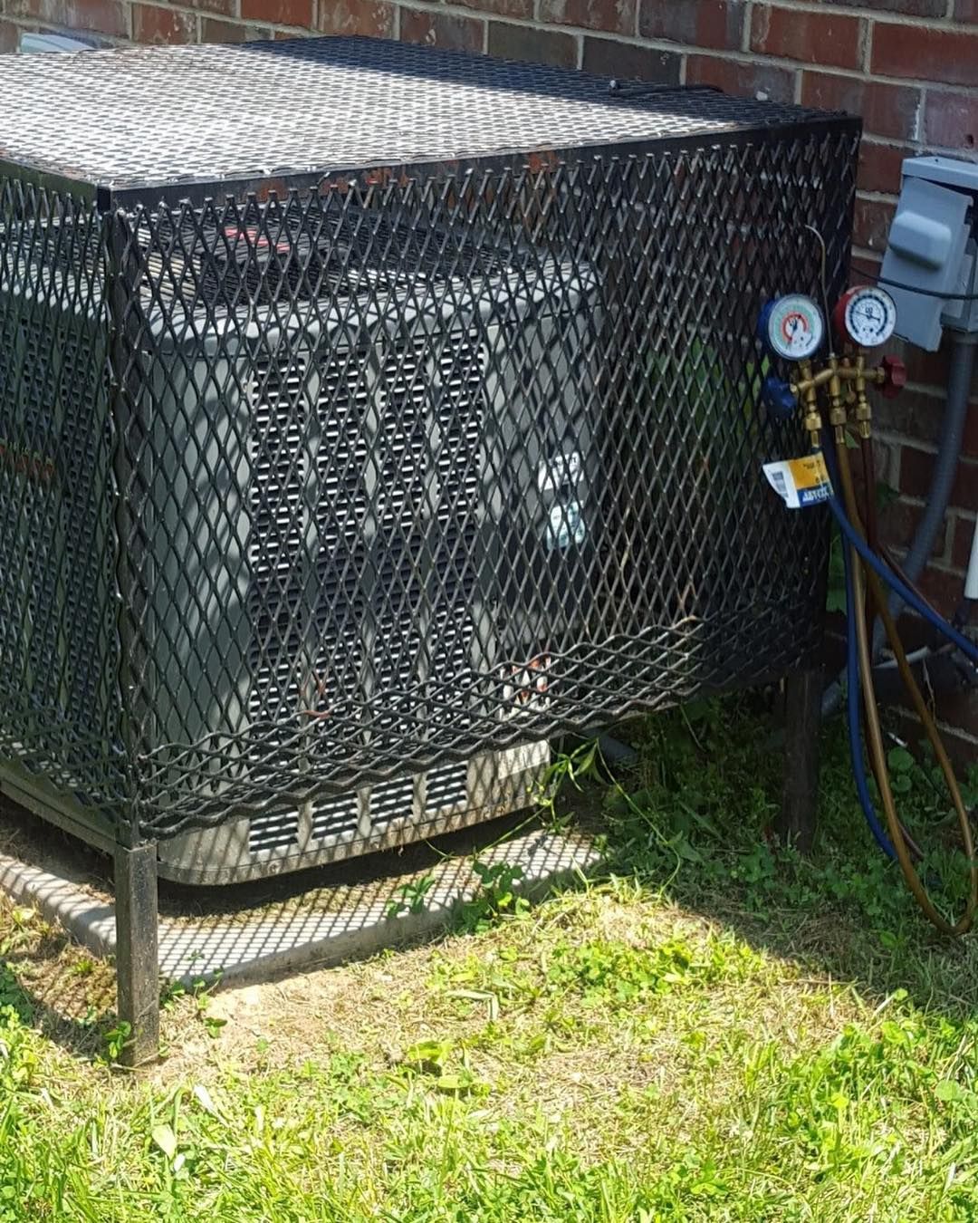 Black mesh cage around an outdoor air conditioning unit next to a brick wall.