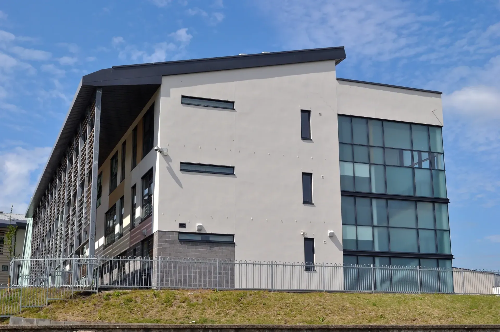 A modern three-story building with white walls, a glass curtain wall, and a decorative metal facade under a blue sky.