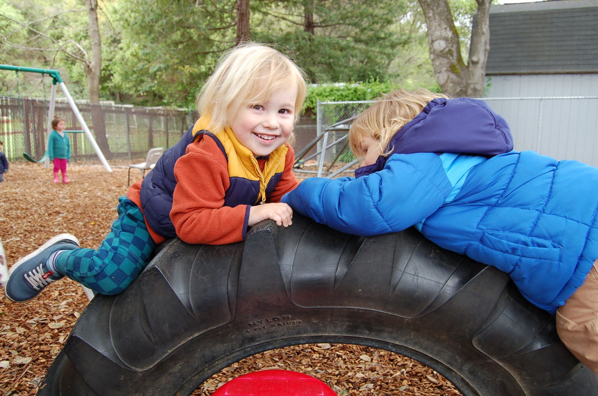Two montessori toddler are playing on a tire at a playground