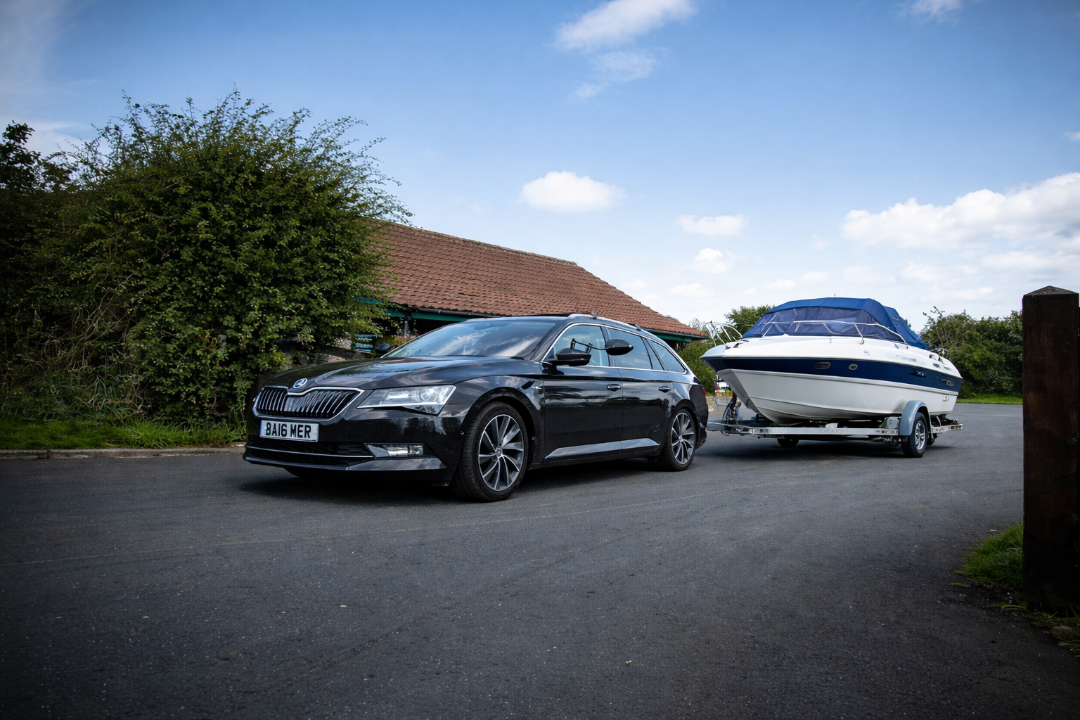 Black car towing a boat on a trailer on a paved road; blue sky in the background.
