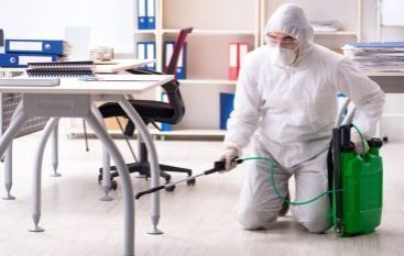 pest control technician in protective gear spraying classroom for bugs