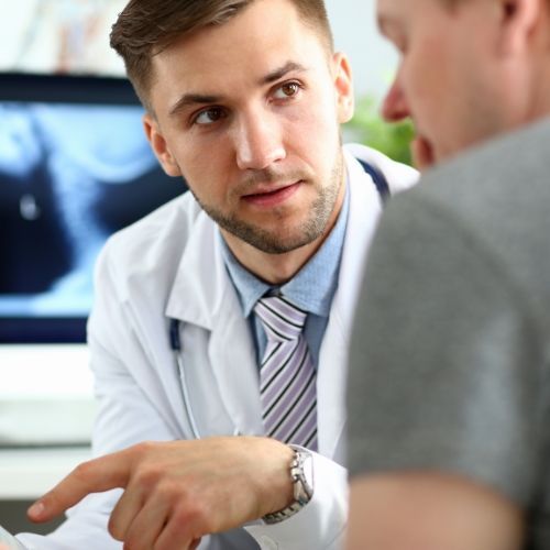 Un médico está hablando con un paciente frente a una pantalla de computadora.