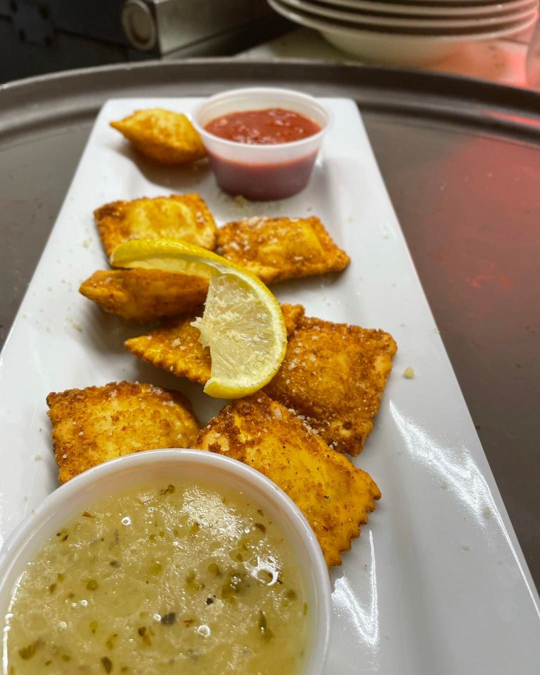 A white plate topped with fried ravioli and dipping sauce.
