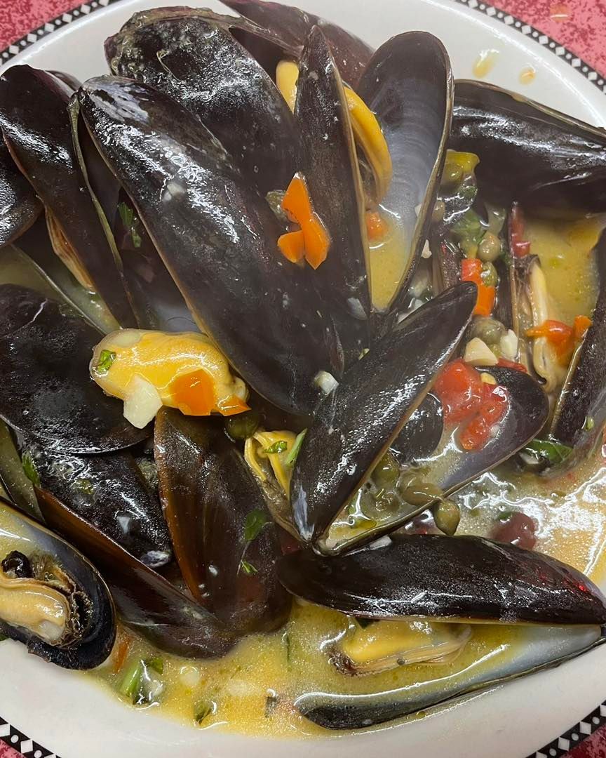 A plate of mussels with sauce and vegetables on a table