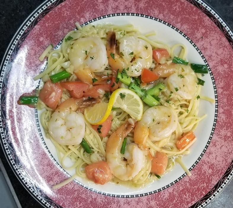A plate of spaghetti with shrimp and vegetables on a table