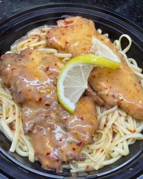A bowl of chicken and noodles with a slice of lemon on top.