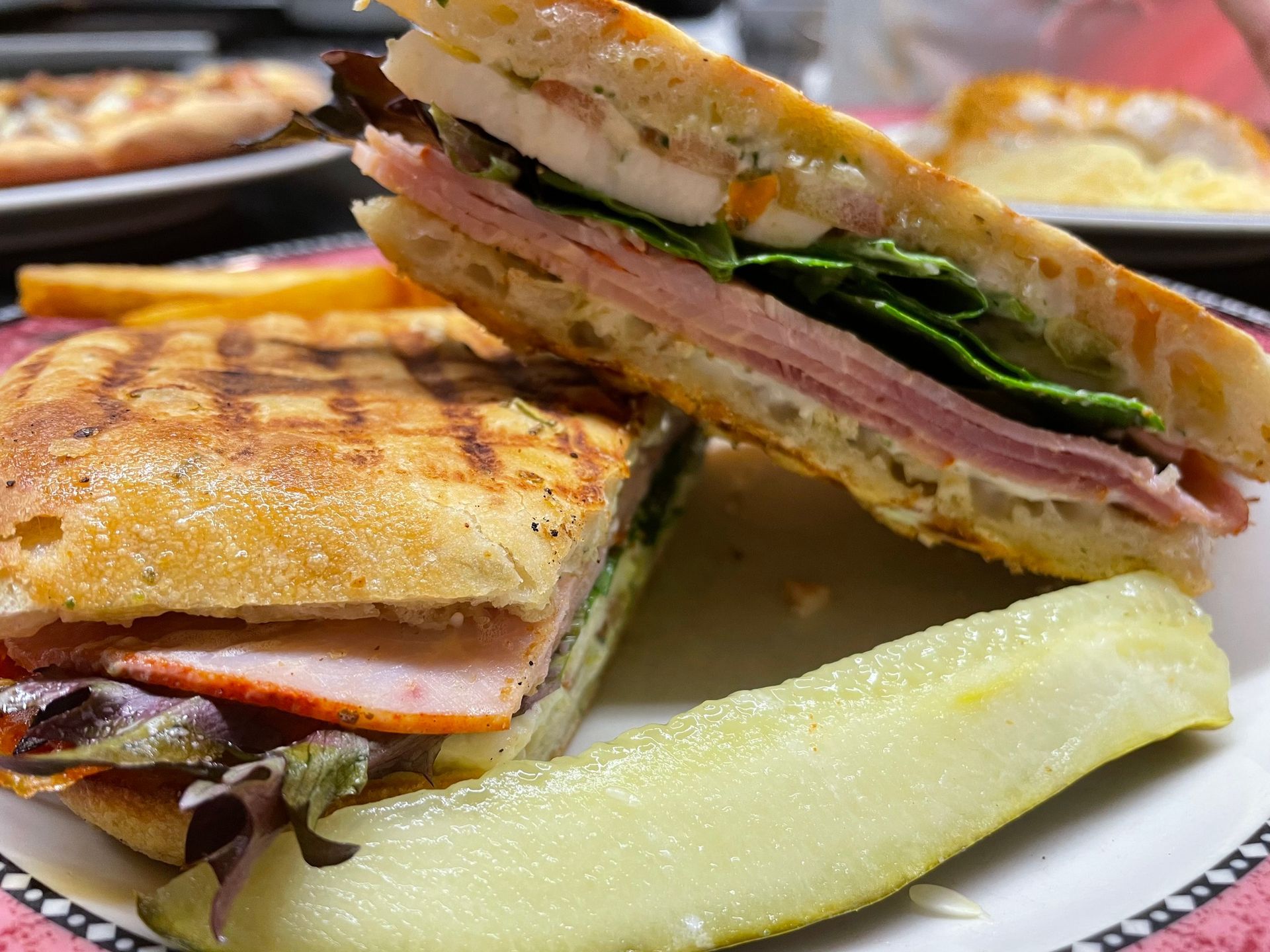 A close up of a sandwich on a plate with french fries and a pickle.