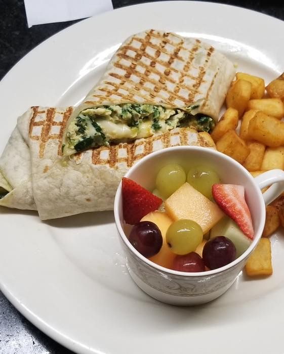 A white plate topped with a wrap french fries and a bowl of fruit