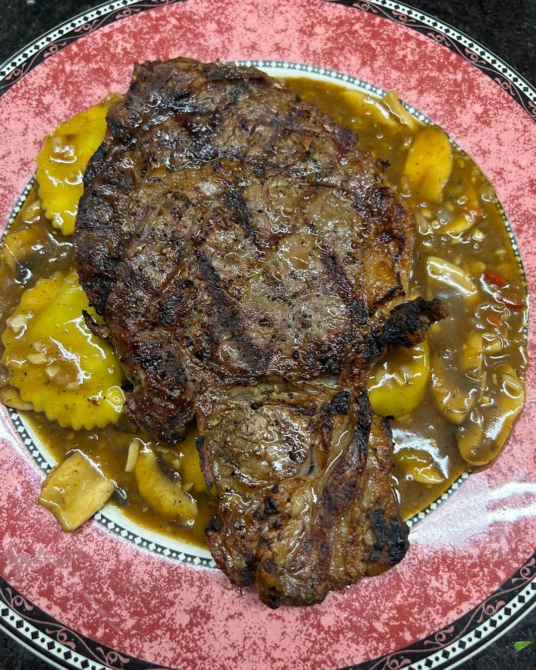 A steak with mushrooms and corn on the cob on a plate.
