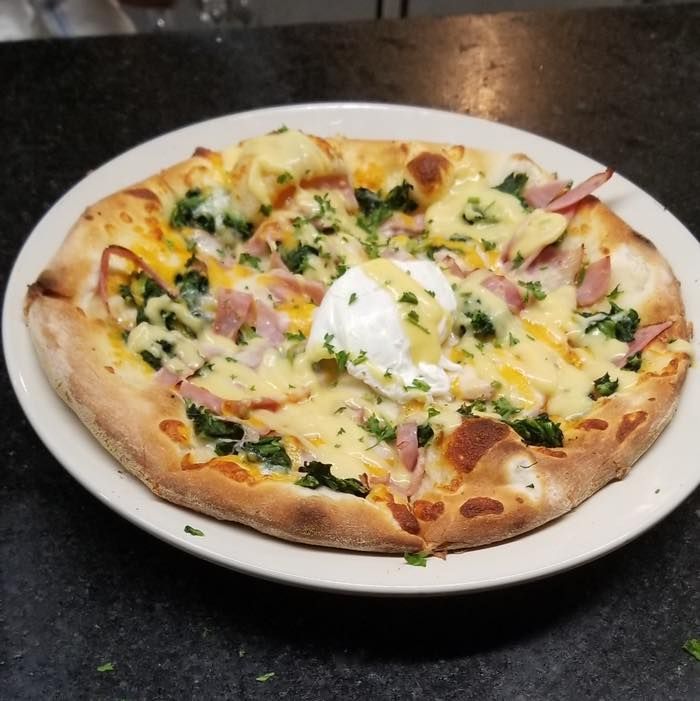 A pizza with a poached egg on top is on a white plate