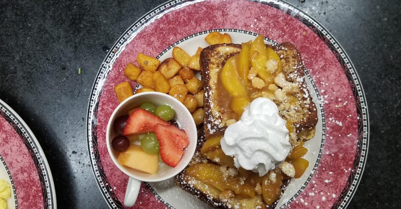 A plate of food with french toast , fruit and whipped cream on a table.