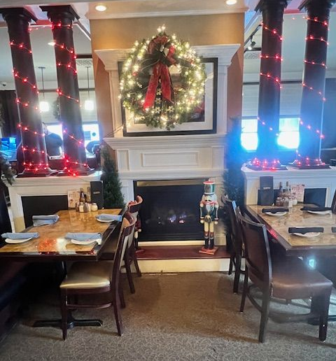 Restaurant dining area with fireplace, holiday wreath, tables, chairs, and festive decorations.