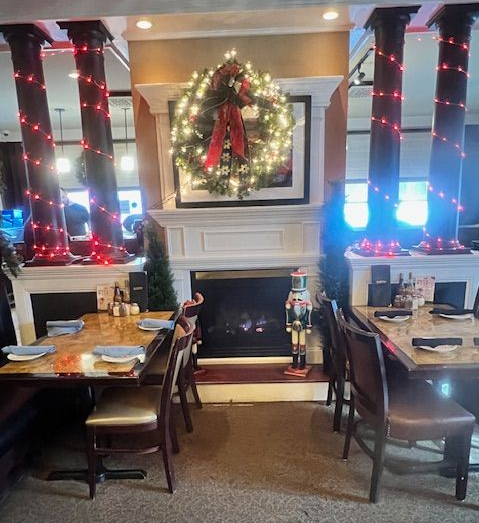 Restaurant interior with fireplace, Christmas wreath, tables, chairs, and festive decorations.