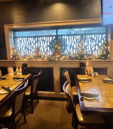 Restaurant interior with tables set for dining, decorated with Christmas garland and small trees.