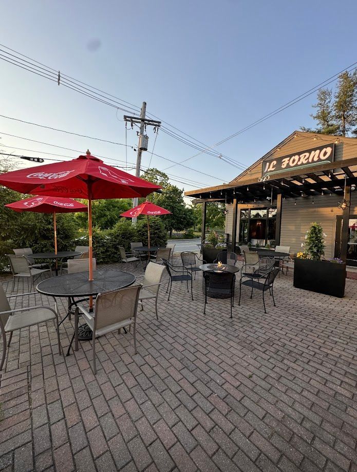 A patio with tables and chairs and red umbrellas in front of a restaurant.