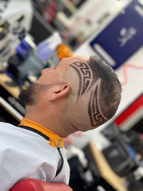 Barber trimming a client’s dark hair in a salon, with a fade haircut in progress