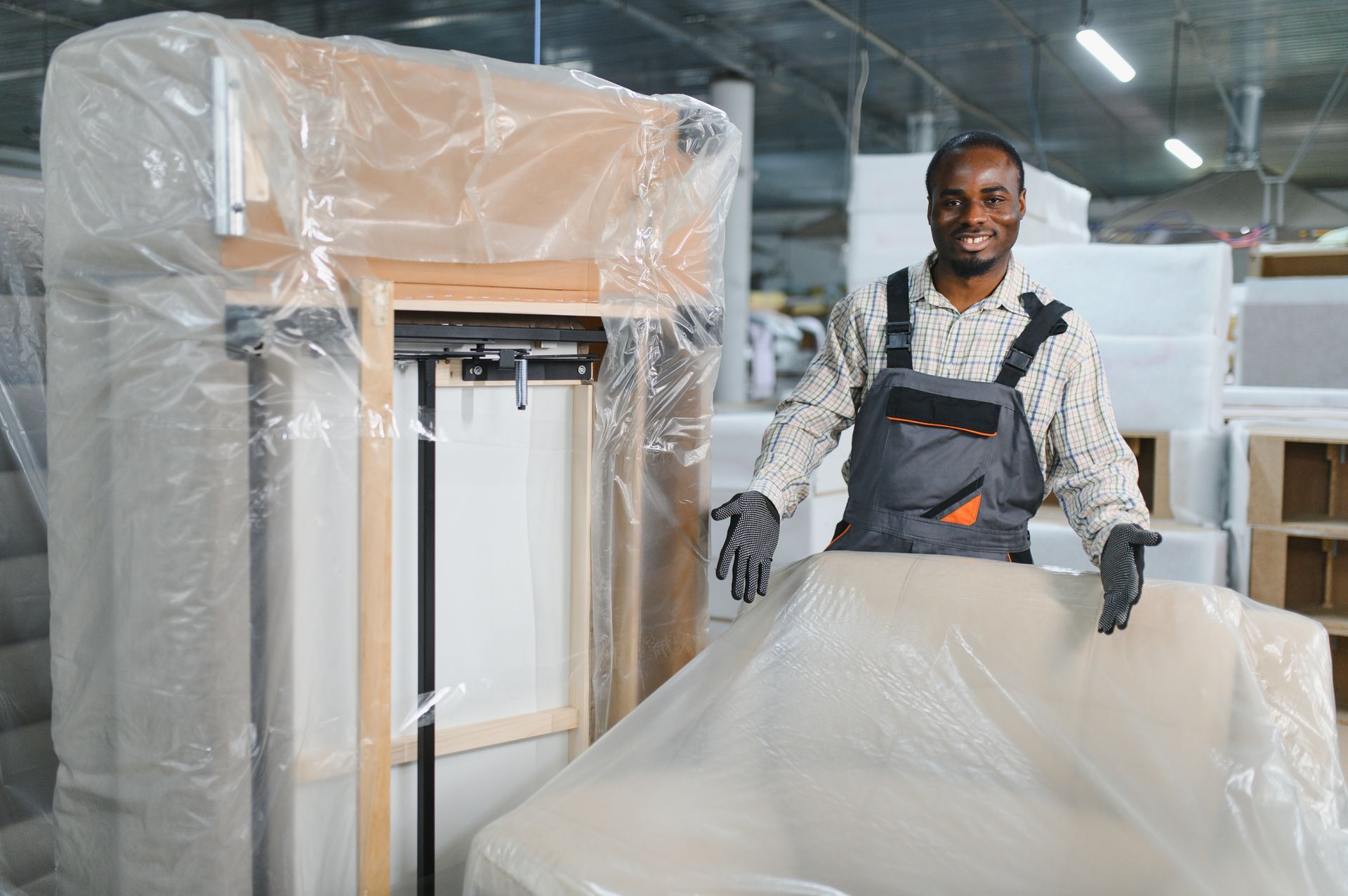 A smiling worker is showing a wrapped sofa in a storage facility, ready to be stored. A smiling worker is showing a wrapped sofa in a storage facility, ready to be stored.