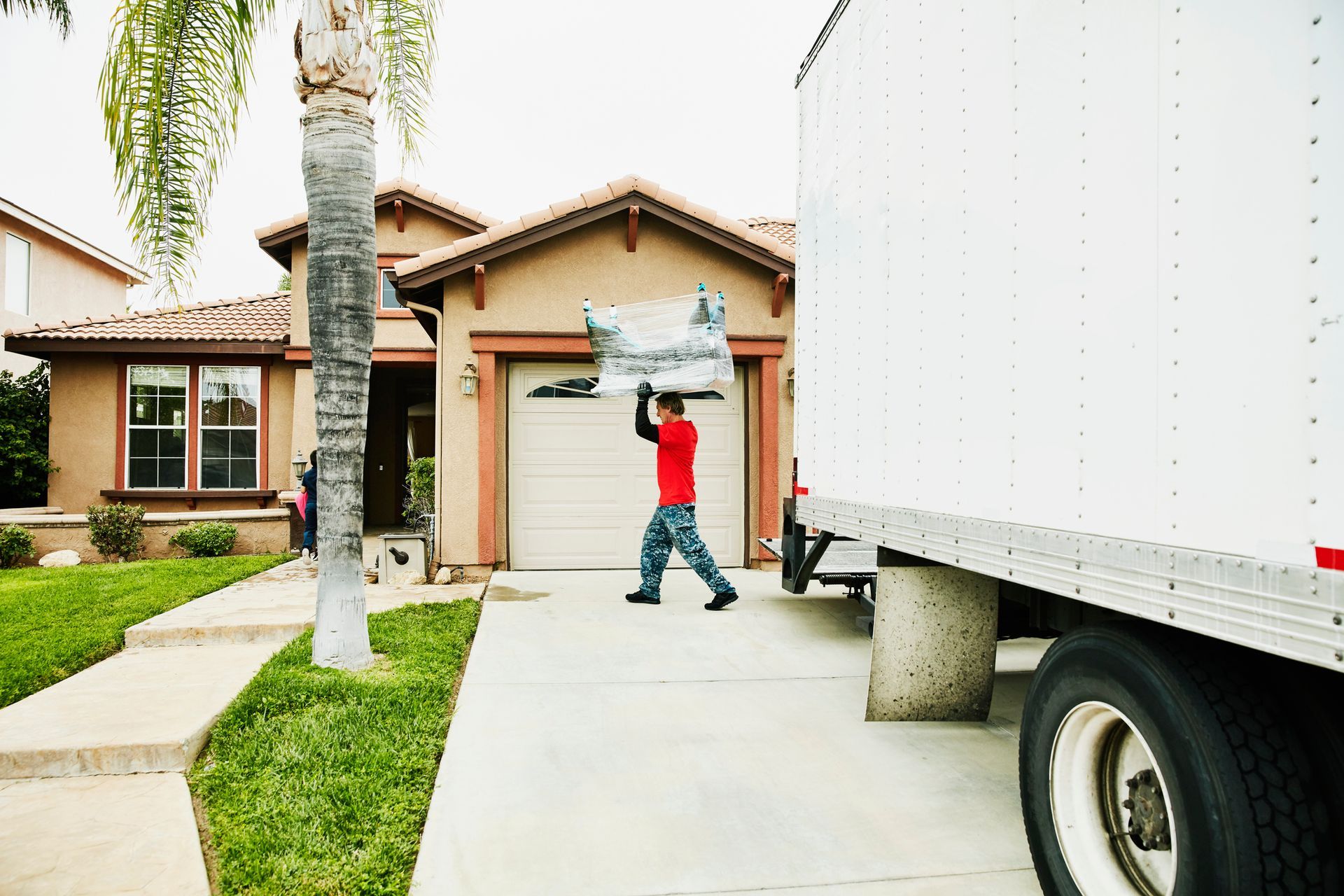 A man is carrying a couch in front of a moving truck.